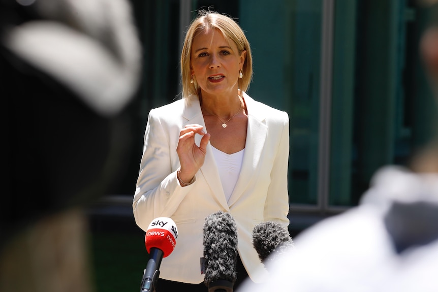 Kristina Keneally wearing a white blazer and blouse mid-sentence standing in a bright courtyard on a sunny day