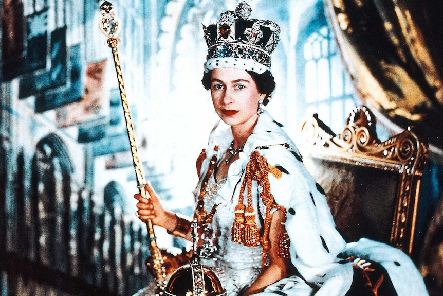 Queen Elizabeth poses in her coronation dress and robe and wearing the Imperial State Crown while holding the Sceptre and Orb.