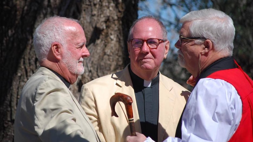 bishop stands in front of two men conducting blessing