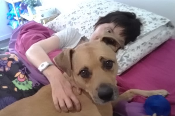 A woman and a dog cuddle up to each other.