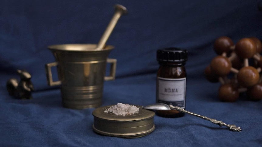 An MDMA bottle with drugs and teaspoon in the foreground.