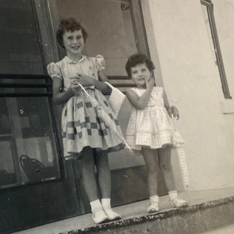 Black and white photo of two little girls standing on a step.