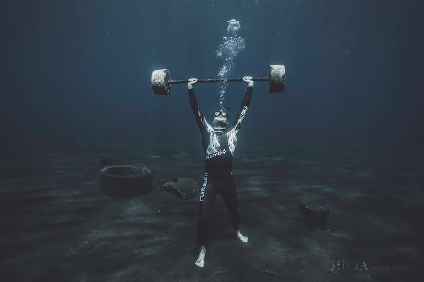 Ant Judge standing on the bottom of the ocean holding gym weights above his head