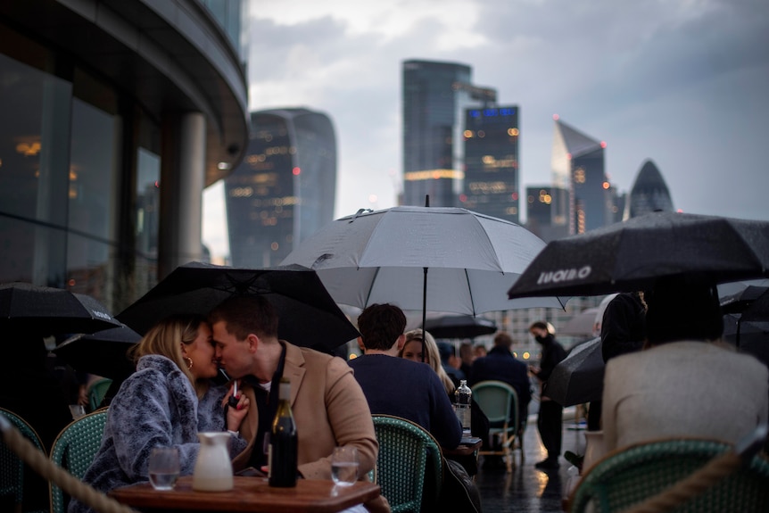 A couple kiss among other patrons holding umbrellas at a restaurant in London