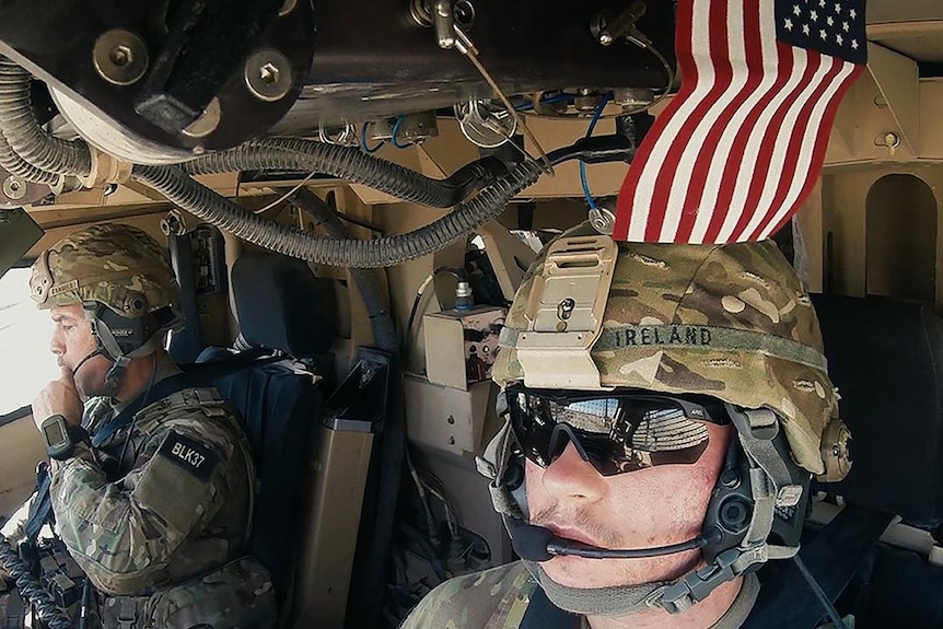 Two US military officers inside a chopper with a small US flag above their heads