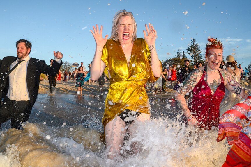 A woman in a gold formal dress splashes into the sunny ocean.