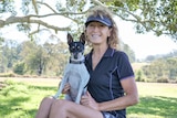 Young woman sits on a lawn smiling with a small dog on her kap.