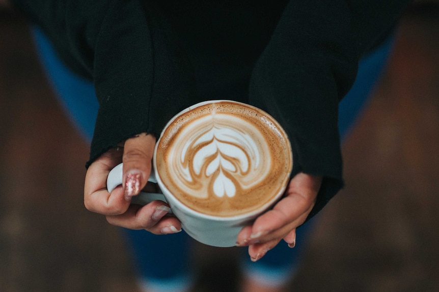 A woman wearing jeans and a black sweater holds a cup of coffee.