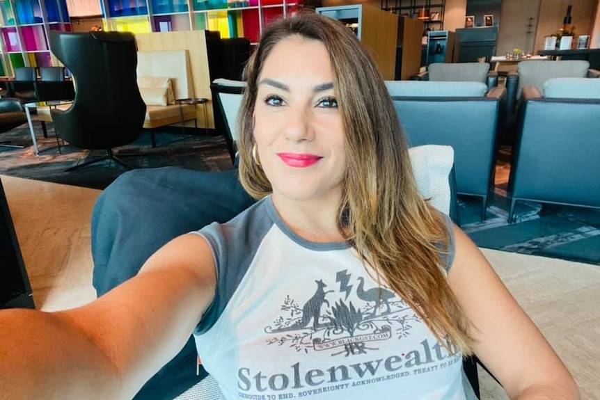 A woman wearing a tshirt that says "stolenwealth" takes a selfie inside a lounge.