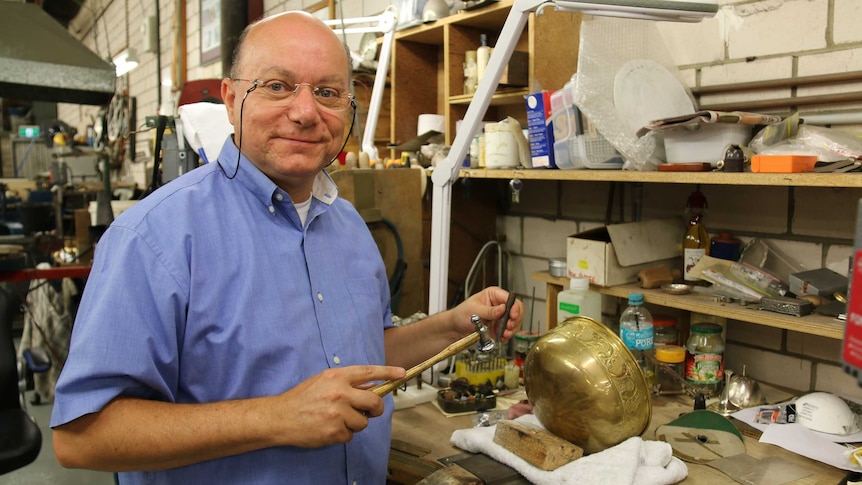 A man poses in a workshop with tools in hand