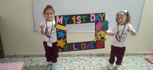Two young kids holding up a sign reading 'My 1st Day'. 