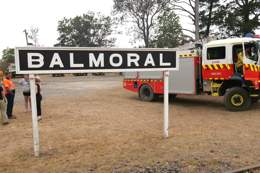 A town sign by the roadside says 'Balmoral'. Behind it a fire truck is parked.