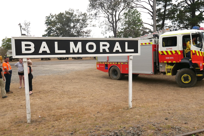 A town sign by the roadside says 'Balmoral'. Behind it a fire truck is parked.