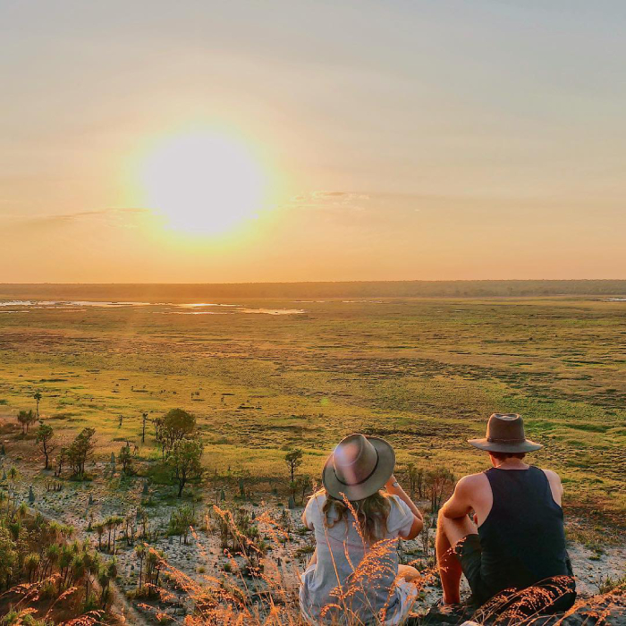 Two people look out across flood plains at sunset.