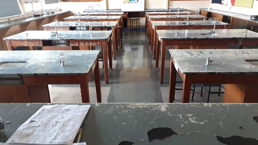 Old, chipped benches with sinks and Bunsen burners are seen from the front of a classroom.