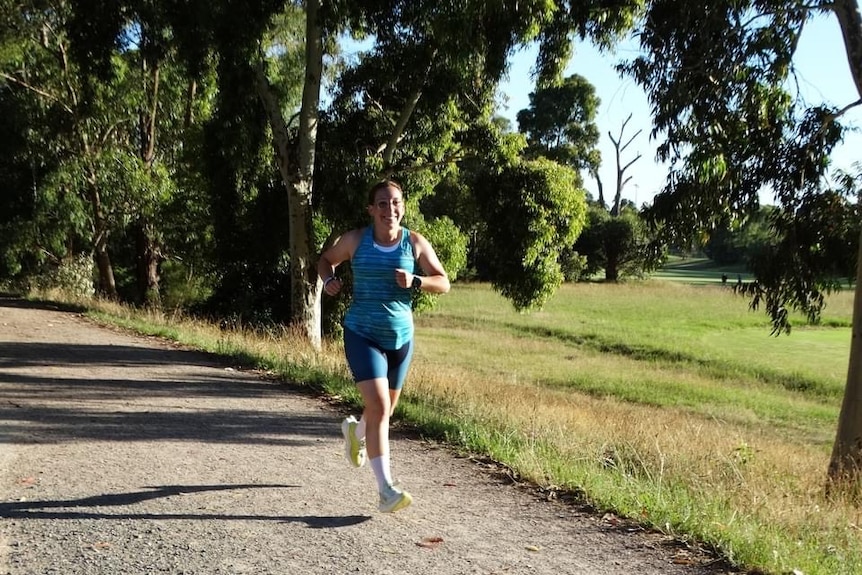 A woman runs along a dirt path with trees and a park surrounding her. She wears a blue running outfit.