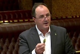 Jeremy Buckingham in a blazer, shirt and glasses holding  green cannabis in his hand
