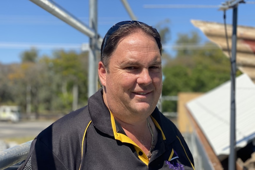 A man smiles. He is wearing a yellow and black polo.