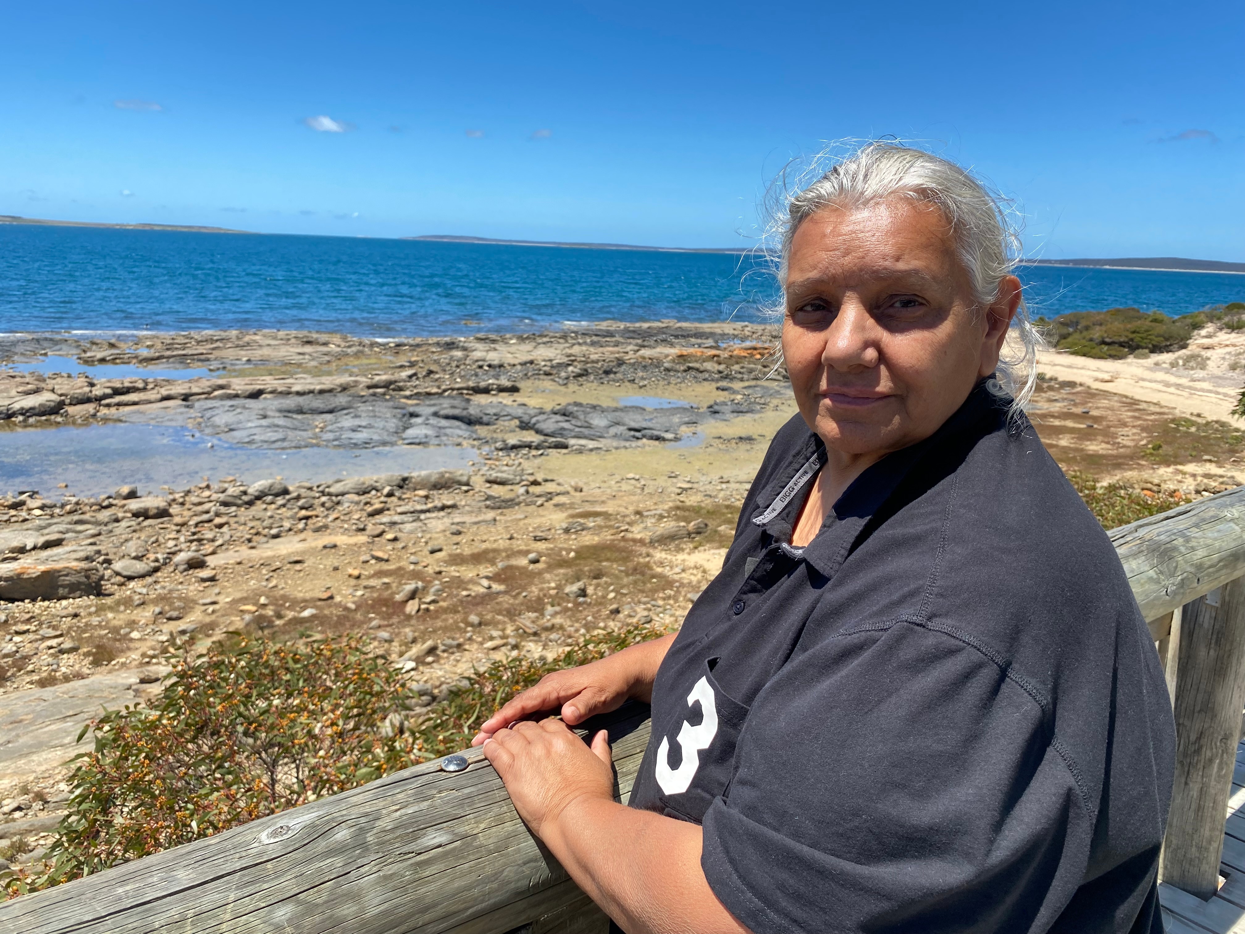 An Indigenous woman in a black polo shirt with grey hair looks at the camera at Billy Lights Point lookout