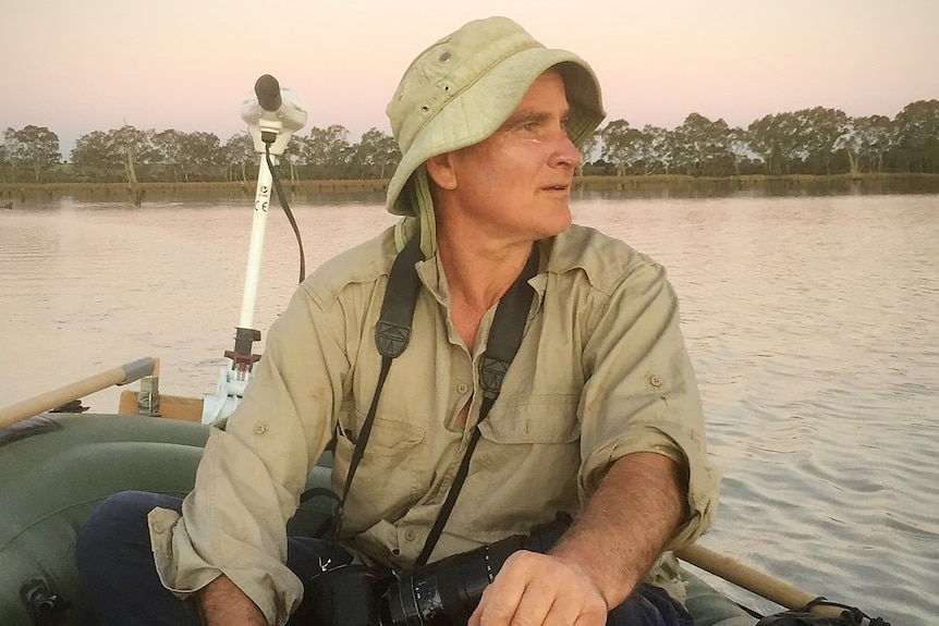 A man in a khaki shirt and slouch hit sits in a boat.
