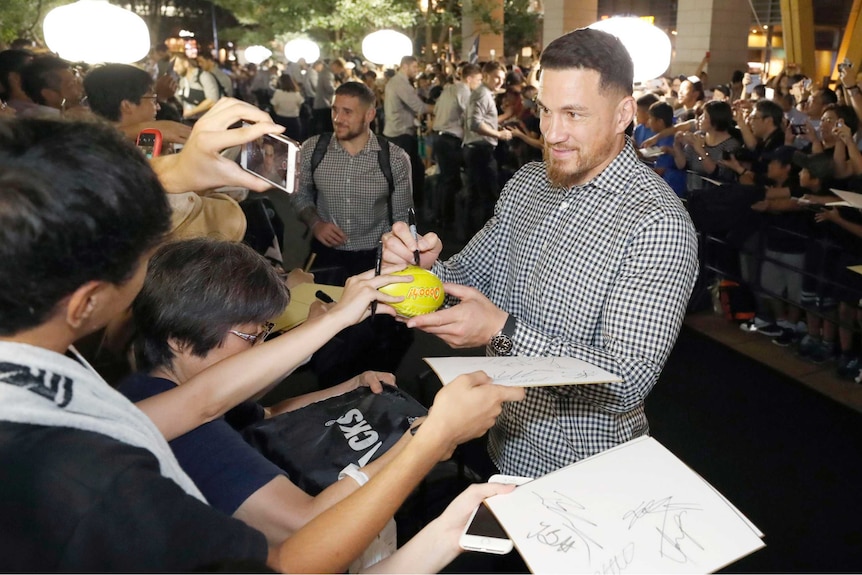 A male rugby union player smiles as he signs an autograph for a fan.