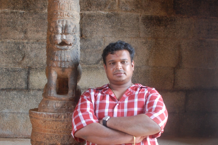 A man stands in a temple next to a carved  stone pillar.