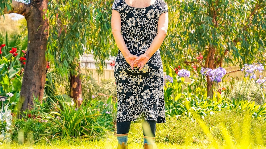 A woman wearing a black and white floral dress stands in a garden with her back to the camera.
