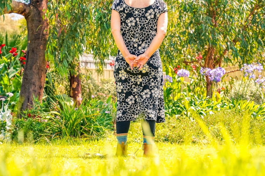 A woman wearing a black and white floral dress stands in a garden with her back to the camera.