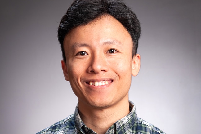 A headshot of a Vietnamese man smiling wearing checked shirt.