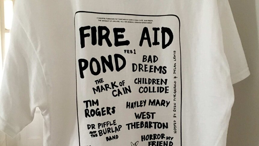 A T-shirt hangs on a door inside a house with a bunch of band names listed on it in large type.