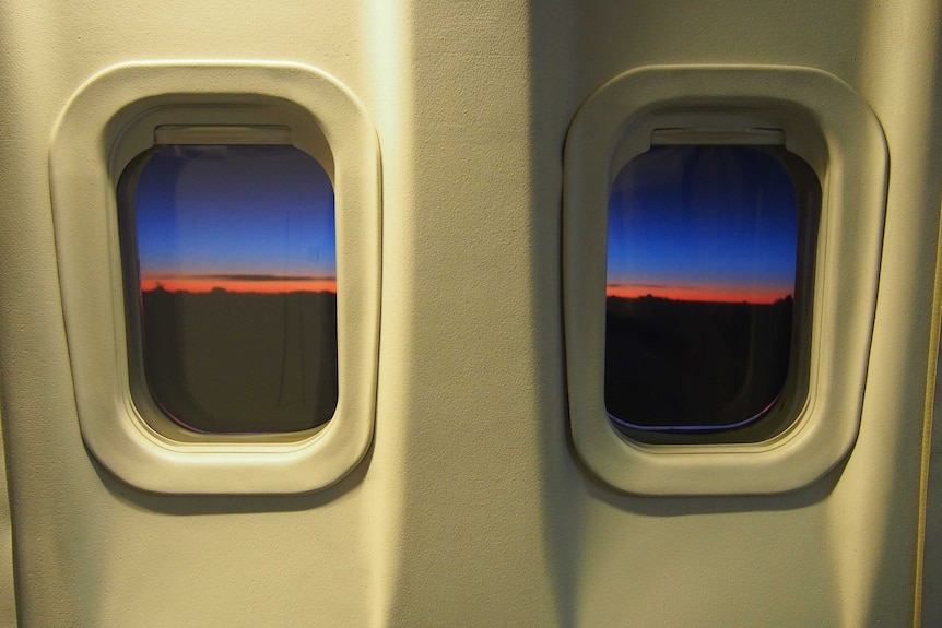 The beginning of a sunrise, seen through two aeroplane windows.