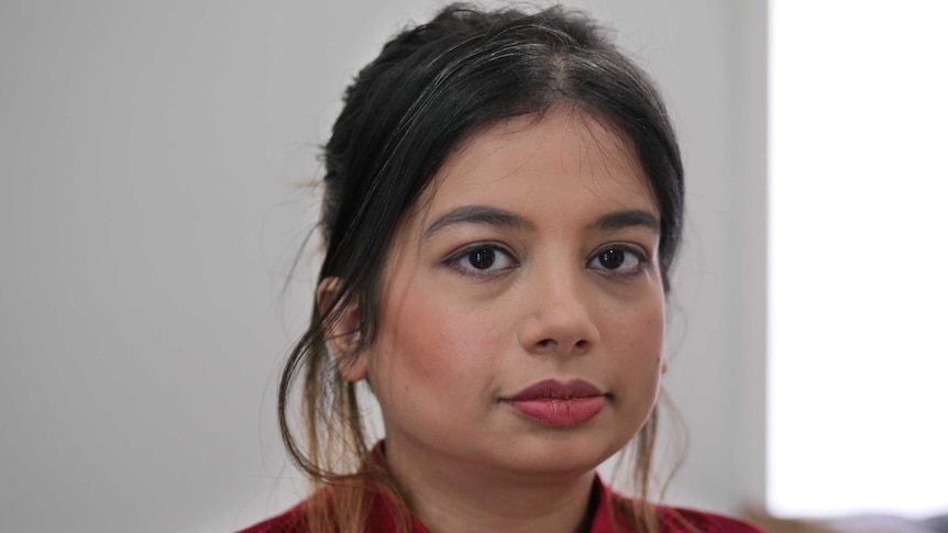 Portrait picture of a young woman of Indian background wearing a dark red top.