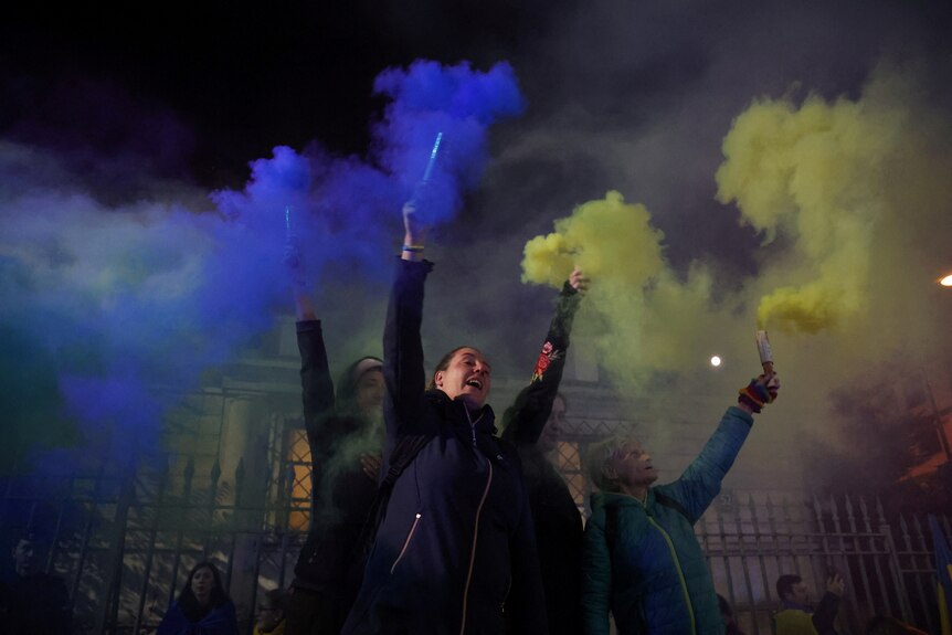 Women hold flares as protestors gather outside the Russian embassy in Warsaw .