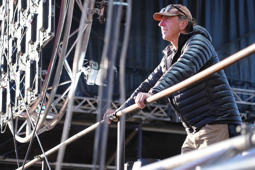 A man wearing a cap and sunglasses leans on a railing.