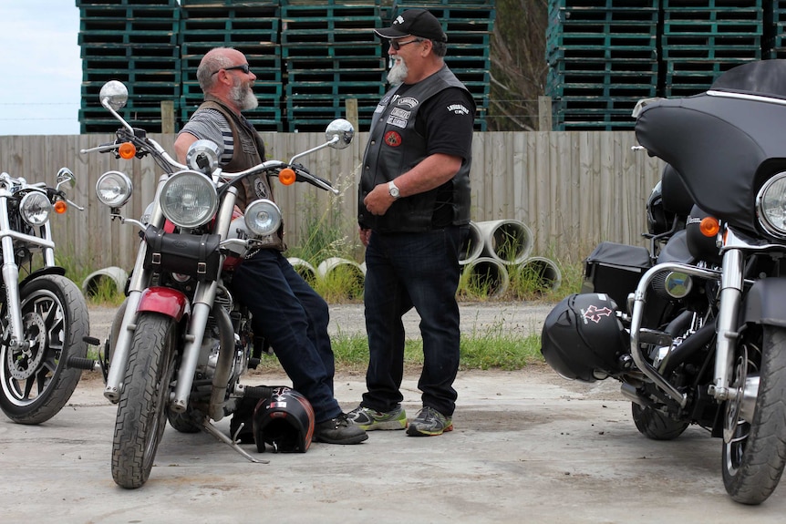 Men leaning against motorbikes talking.