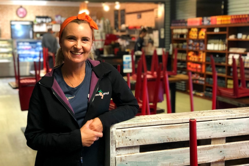 A woman wearing an orange headband stands leaning on a crate in a near-empty cafe.