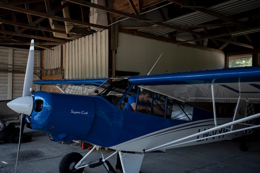 a blue and white small aircraft is parked in a shed with a man inside