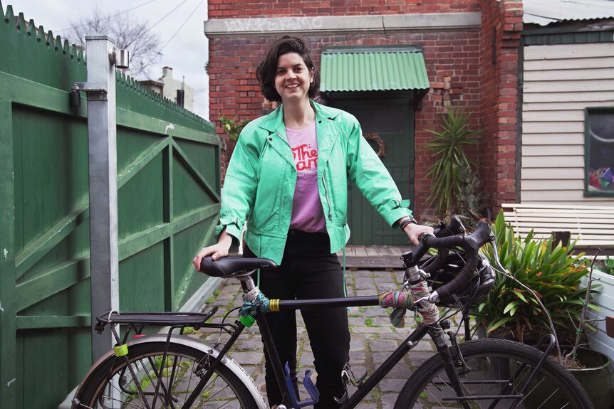 Cyclist Julia stands in her backyard holding her bike, she's smiling.