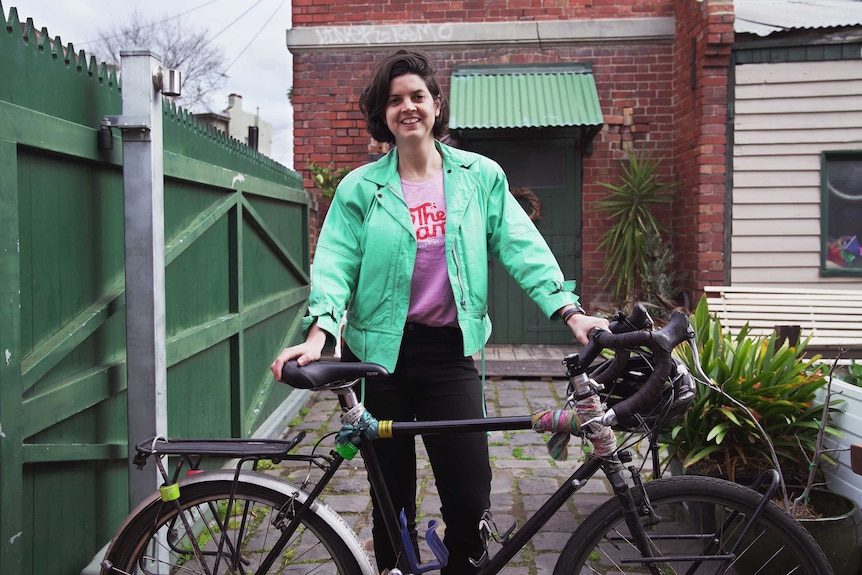 Cyclist Julia stands in her backyard holding her bike, she's smiling.