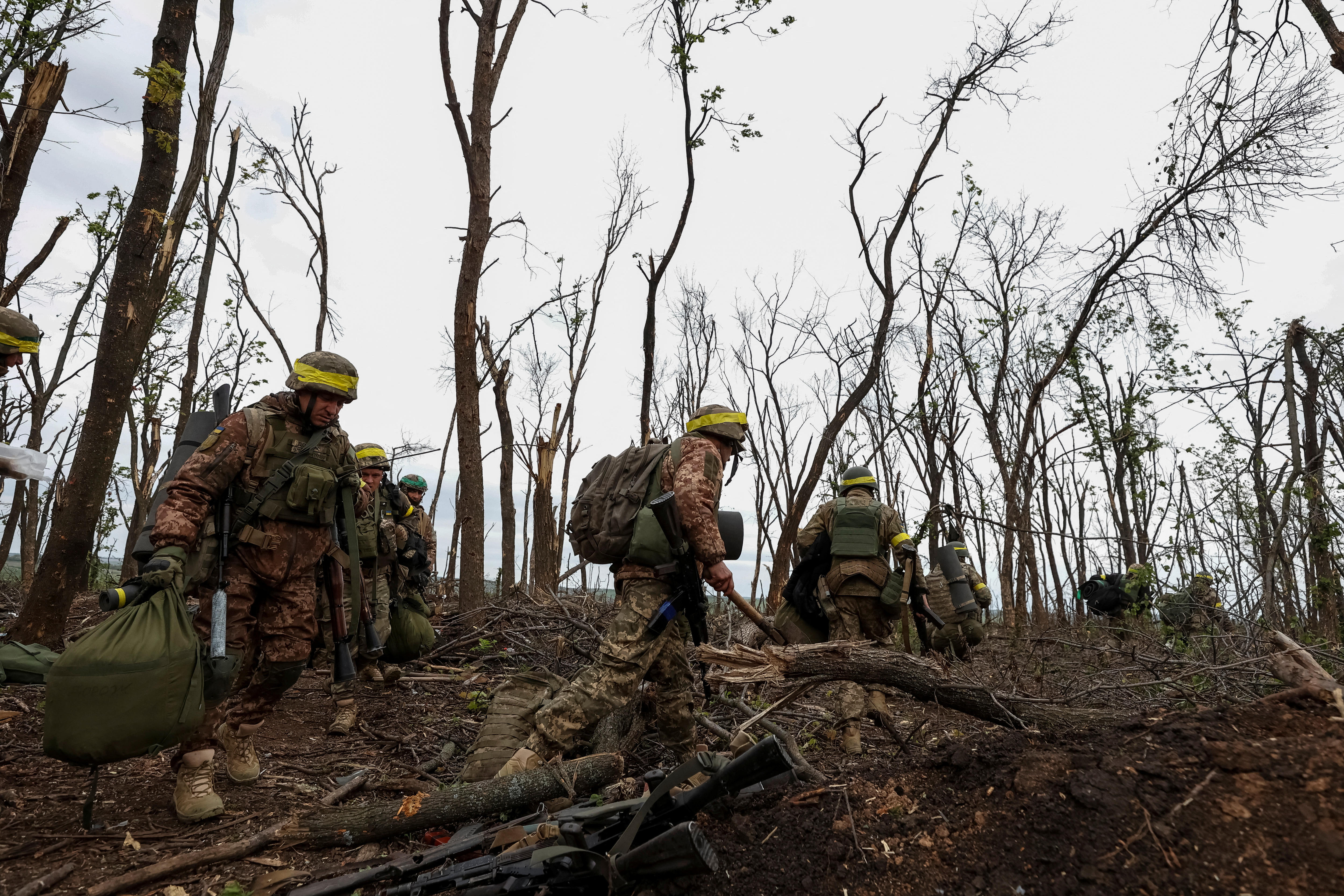 Ukrainian servicemen walk after a fight near the front line city of Bakhmut. The Sky is grey and there are no leaves on trees.