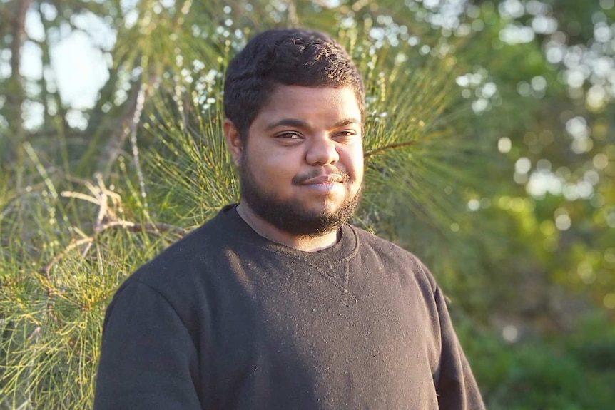 A man with curly black hair and a black beard smiles at the camera.