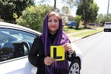 Learner driver Behnaz Sadeghi, 37, stands beside a car holding a L-plate sign