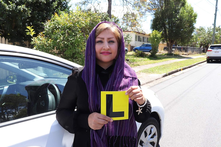 Learner driver Behnaz Sadeghi, 37, stands beside a car holding a L-plate sign