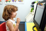 A young girl sits at a desk and looks at a computer screen inside a kids room.