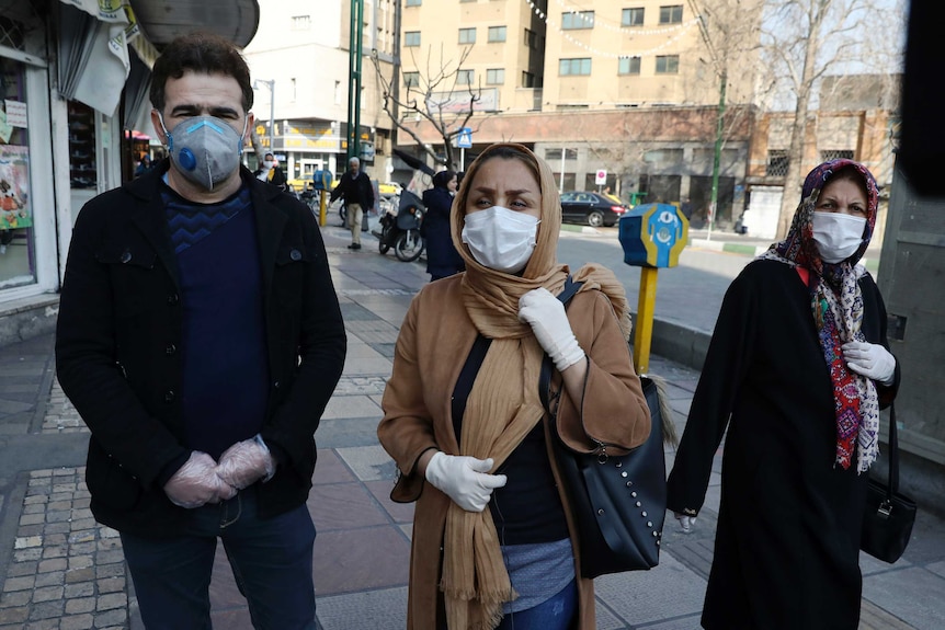 Three people wear masks and surgical gloves as they stand in the street.