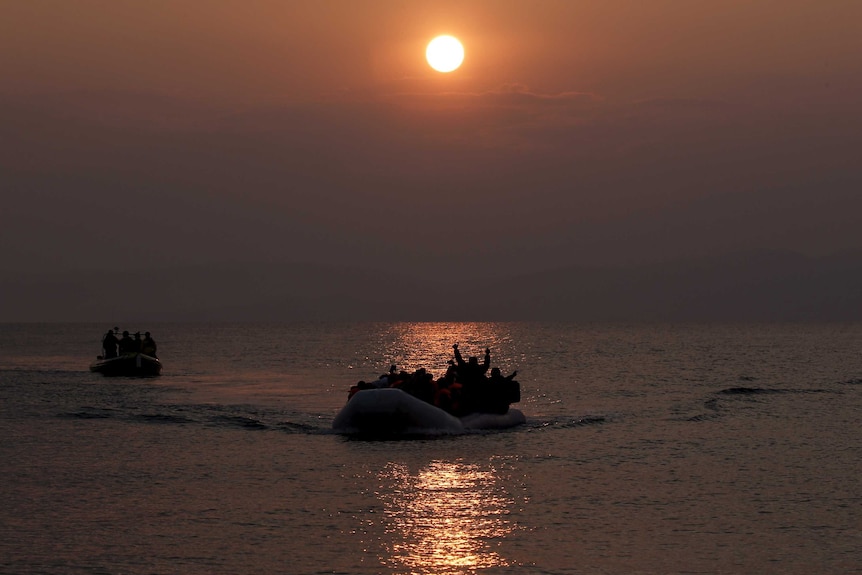 Asylum seekers wave as they approach the shores of Lesbos on a dinghy.