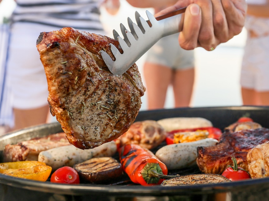 A steak being cooked on a barbecue on a sunny day.