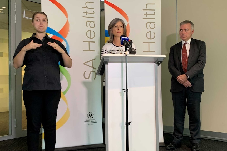 A woman stands at a podium with a woman on one side and a man on the right