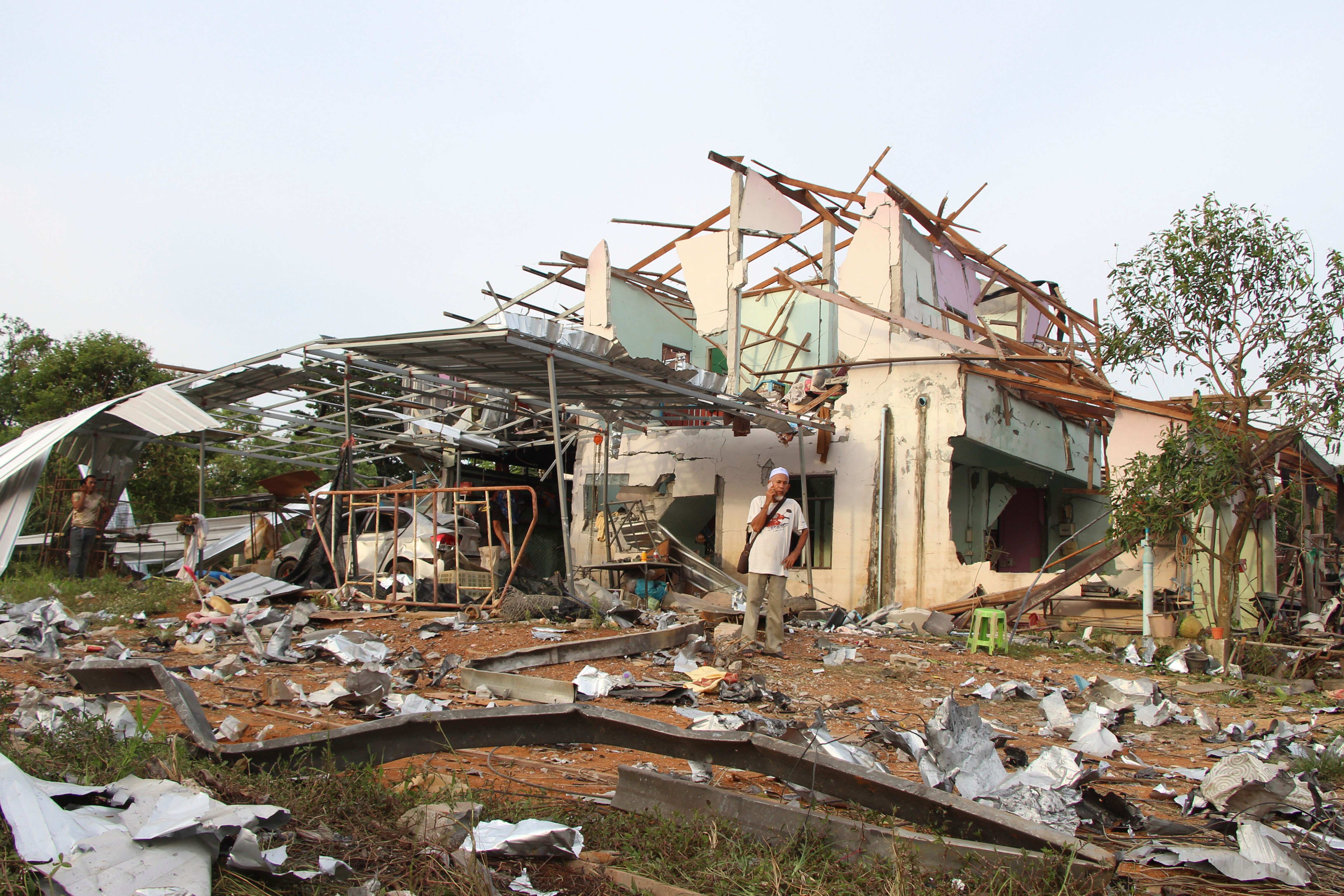 People speak on their phones in front of a house damaged by an explosion at a firework warehouse .