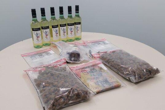 Cannabis and cash in zip lock bags and bottles of wine sit on a  table.